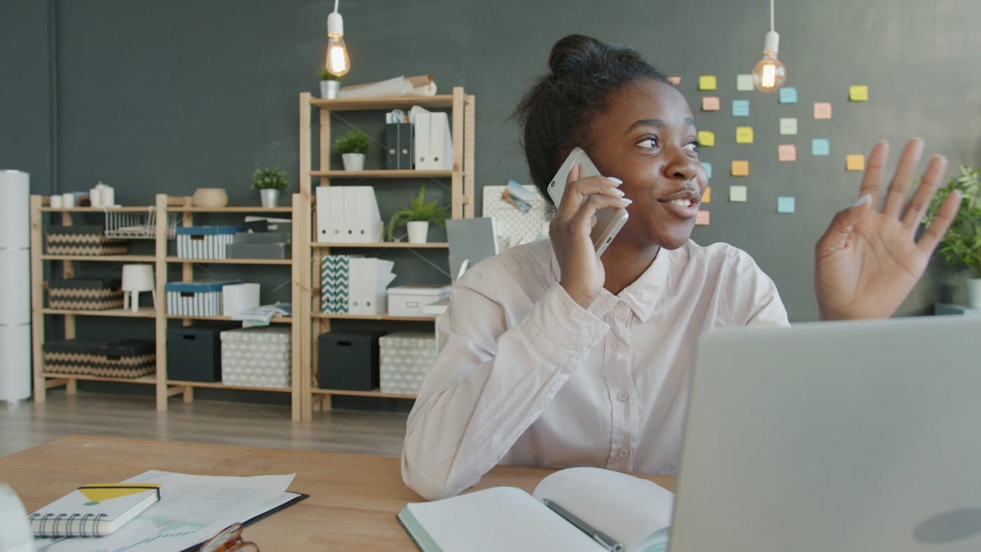 Young woman talking on phone at desk with laptop